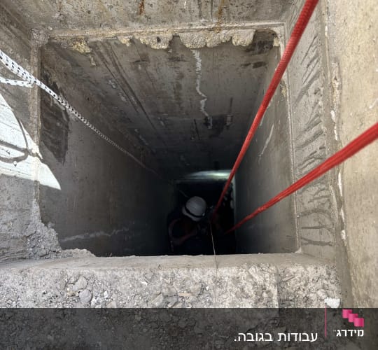 איש מקצוע מבצע עבודה בגלישת חבלים (סנפלינג) בתוך פיר בטון עמוק